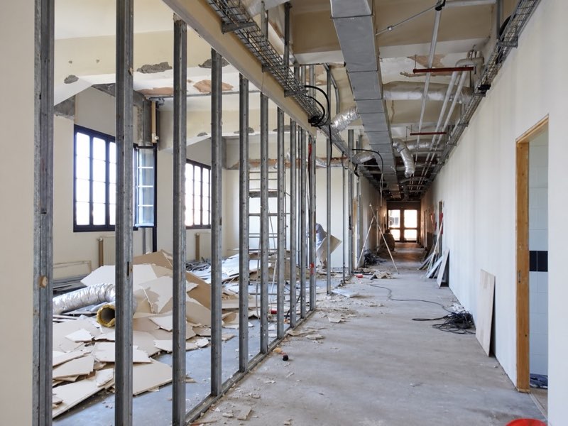 Corridoio interno in fase di demolizione e ristrutturazione, con struttura metallica a vista e materiali di risulta