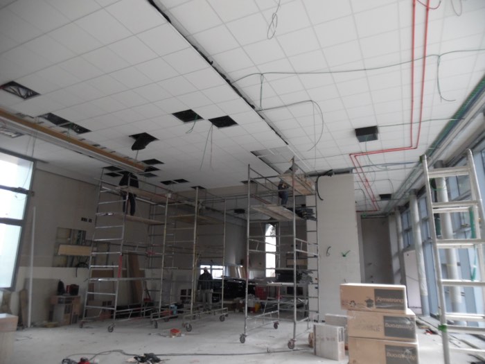 Cantiere aperto con ponteggi durante un intervento su controsoffitto e impianti tecnologici interni in un edificio industriale