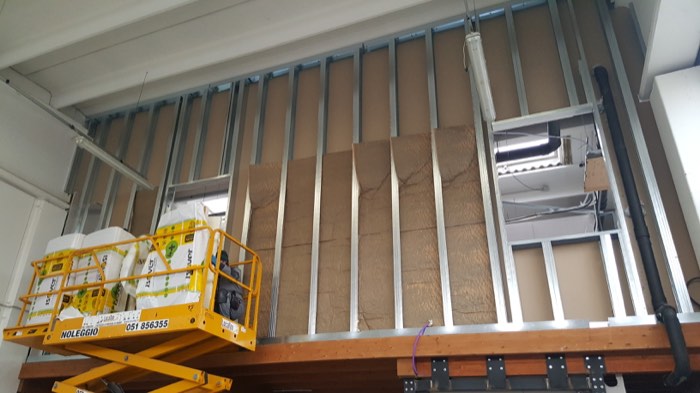 Struttura metallica e pannello isolante durante un intervento interno in un edificio industriale, con piattaforma elevatrice