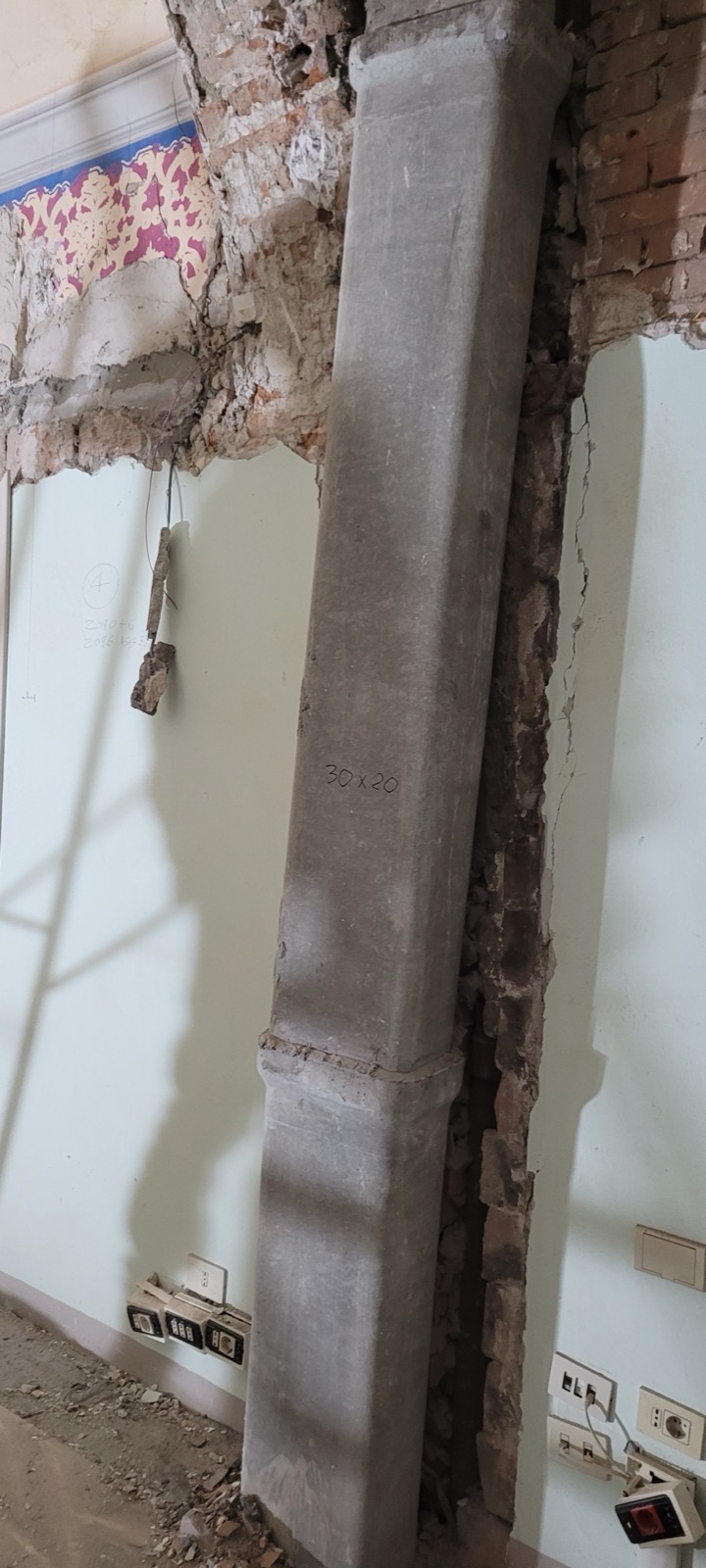 Nuovo pilastro in cemento armato inserito in un'apertura di muratura storica, con un frammento di carta da parati decorata visibile sopra
