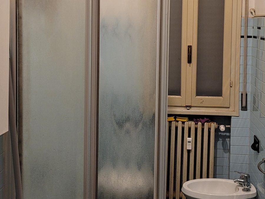 Bagno datato con box doccia in alluminio, piastrelle anni '70-'80 e impianti da rifare, prima della ristrutturazione